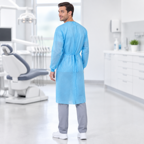 Man wearing a blue disposable isolation gown in a dental clinic, showing the back and waist tie.
